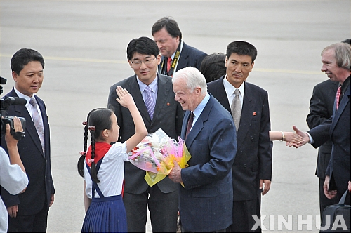 【평양(북한)=신화/뉴시스】북한을 방문한 지미 카터 前 미국 대통령(오른쪽)이 25일 평양 공항에 도착, 환영나온 북한 어린이로부터 인사를 받고 있다.&nbsp;&nbsp; 카터 前 대통령은 현재 북한에 억류돼 있는 미국인 곰즈(Aijalon Mahli Gomes)의 석방 논의를 위해 25일 평양을 방문했다.&nbsp;&nbsp; 