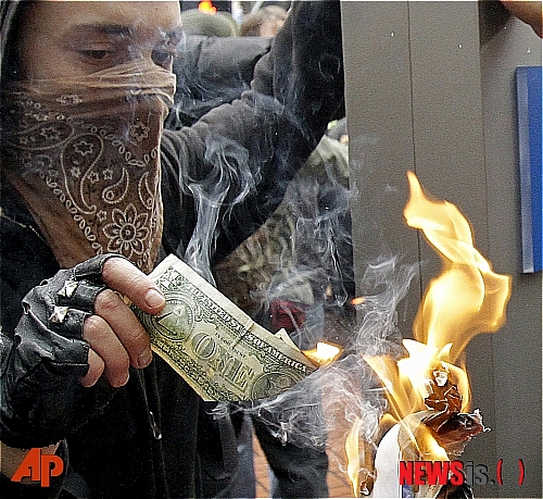 【포틀랜드(미 오리건주)=AP/뉴시스】미 오리건주 포틀랜드의 뱅크 오브 아메리카 건물 앞에서 반월가 시위에 참여한 한 시위자가 1달러 지폐를 불태우고 있다. 이날 반월가 시위 발생 두 달을 맞아 미국 주요 도시들에서 일제히 반월가 시위가 대규모로 열렸다.