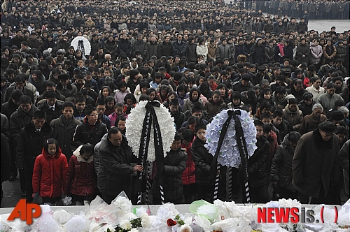 【평양=AP/뉴시스】평양 시민들이 21일 평양실내체육관 앞 광장에 내걸린 김정일 북한 국방위원장의 대형 사진 앞에 애도를 표하기 위해 길게 줄을 지어 모여 있다.