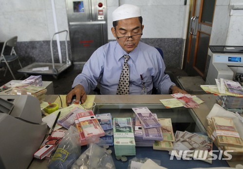 【자카르타=AP/뉴시스】 인도네시아 중앙은행은 오는 30일 추가 통화정책회의를 개최한다고 29일 밝혔다. 이번 회의는 루피아화 가치 급락에 따라 열리게 된다. 사진은 지난 2012년 8월 1일 자카르타 인도네시아 중앙은행에서 한 직원이 루피아 다발을 책상위에 두고 일하는 모습. 2018. 5.29