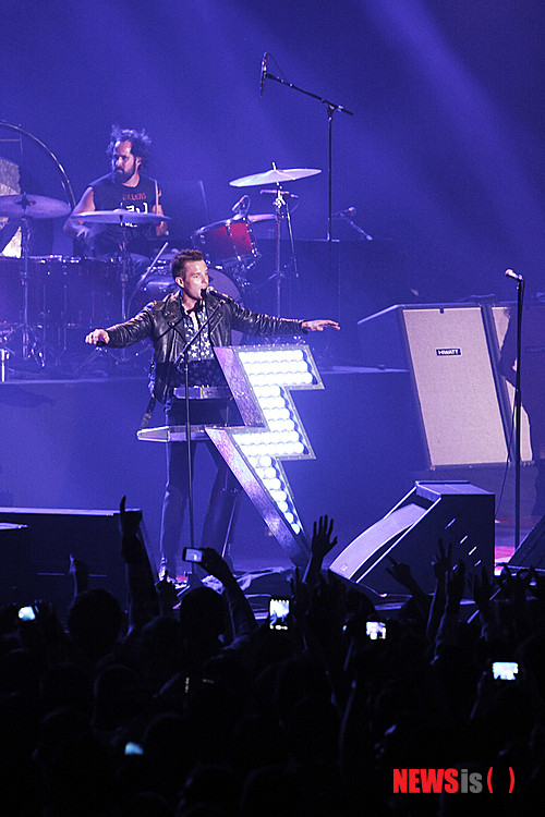 【서울=뉴시스】이재훈 기자 = "아이 갓 솔, 벗 아임 낫 어 솔저. 아 갓 솔, 벗 아임 낫 어 솔저(I got soul, but I'm not a soldier) ♩♬'….&nbsp; '올 디즈 싱스 댓 아이브 돈(Alll these things that I've done)'이 5일 밤 서울 올림픽공원 올림픽홀에서 울려 퍼지자 약 3400명은 모두 약속이나 한 듯 따라 불렀다. 인터넷에서 이벤트를 논의한 일부 팬들은 지퍼 백에 담아온 종이 가루를 노랫말에 맞춰 흩뿌리기도 했다.&nbsp;&nbsp; 미국의 록밴드 '더 킬러스(The Killers)'의 첫 내한공연 '현대카드 컬처프로젝트 12 더 킬러스'는 한바탕 록 페스티벌 전쟁이 벌어진 지난 여름의 어떤 공연에도 뒤지지 않을 만큼 열정적이었다.&nbsp; 2004년 데뷔한 킬러스는 애초 2010년 2월6일 첫 내한공연을 할 예정이었다. 그러나 콘서트를 앞두고 보컬 브랜든 플라워스(32)의 모친이 갑자기 사망하면서 취소됐다.&nbsp; 지난해 발매한 정규앨범 '배틀 본(Battle Born)'을 기념하는 투어인 이번 무대는 그간 3년8개월의 기다림을 불식시키기도 남았다. 데뷔년도로 따지면, 기다림이 9년인데 그 아쉬움도 달래줬다. 예정보다 약 20분 늦은 오후 8시20분부터 90여분간 17곡을 들려주며 사운드를 휘몰아쳤다.&nbsp; '배틀본' 재킷 한가운데는 번개가 박혀 있다. 이번 투어 무대의 플라워스가 사용하는 키보드 앞에도 역시 이 번개와 모양이 같은 전열등이 설치됐다. 공연 내내 붉은 색, 푸른 색 등 시시각각 변하며 분위기를 강렬하게 주도했다. 킬러스는 미국 밴드이나, 브릿팝의 멜로디컬한 세련됨 때문에 영국 밴드로 오해를 받는다. 실제 접한 무대 자체는 미국 록밴드들의 테스토스테론이 풍겨나왔다.&nbsp;&nbsp; 사실 '떼창'은 첫곡부터 시작됐다. 킬러스의 대표곡인 '미스터. 브라이트사이드(Mr. Brightside)'로 예열을 할 필요도 없이 바로 끓는 점으로 돌입했다. 다만 이 곡의 제목처럼 객석의 조명은 꺼지지 않았다. 2번째 곡 '스페이스맨'부터 객석의 조명이 꺼지고, 번개가 반짝이기 시작했다.&nbsp;&nbsp; '프럼 히어 온 아웃'을 부른 뒤에는 다소 엄숙했다. 플라워스가 하늘에 있는 어머니를 떠올렸기 때문이다. 2010년 첫 내한공연을 취소할 수밖에 없었던 이유다. 플라워스는 이어서 부른 '더스트랜드 페어리 테일' 끝에 눈시울을 붉히기도 했다. 이 곡의 노랫말은 그가 자신의 어머니와 아버지를 신데렐라와 미국 왕자에 비유, 일종의 '황무지의 동화'로 풀어냈다.&nbsp;&nbsp; 플라워스는 그래도 공연의 대부분을 화려한 무대 매너로 팬들을 열광케 했다. 이름 때문에 국내 팬들에게 '브랜든 꽃'으로 통하는 그는 여전히 뛰어난 외모와 세련된 패션 감각을 자랑했다. 초반에 다소 컨디션이 좋아 보이지 않았으나, 한국 팬의 인장과도 같은 뜨거운 반응에 점차 기력을 되찾았다. 내내 모니터용 스피커에 올라가면서 고군부투했다. 서툰 한국말로 "음악과 우리는 너의 것이다"라고 말하는 등 팬들과 소통하려는 모습도 인상적이었다.&nbsp; 이날 플라워스 만큼 빛난 것은 드러머 로니 배누치 주니어(36)였다. 한가운데 자신이 이름이 한글로 적힌 검은 반소매 티셔를 입고 등장, 초반부터 팬들의 환심을 산 그는 '파워 드럼'을 보여주면서 존재감을 확실히 했다. 기타리스트 데이브 큐닝(36)도 자기 몫을 묵묵히 해냈다.&nbsp; 다만, 베이시스트 마크 스토머(36)는 개인 사정으로 이번 내한에 함께 하지 못했다. 대신 공식 투어팀의 연주자가 베이스 연주를 맡았다. 묵직한 베이스 리프가 인상적인 '제니 워스 어 프렌드 오브 마인(Jenny was a friend of mine)'를 스토머의 연주로 듣지 못한 점은 아쉬웠지만 공연의 질에는 크게 문제가 없었다.&nbsp; '제니 워스 어 프렌드 오브 마인' '웬 유 아 영' 등을 앙코르로 들려준 킬러스는 가을 밤, 록이 여름의 전유물이 아니라는 것을 증명했다. 무대 위 번개는 같은 시간 벌어진 '여의도 불꽃 축제'만큼 번쩍였다.&nbsp; 공연에 앞서 실험적이면서도 서정적인 사운드를 선보이는 인디밴드 '3호선 버터플라이'가 오프닝 무대를 꾸몄다. 보컬 남상아(40)는 '헤어지는 날 바로 오늘' '내가 고백을 하면 깜짝 놀랄거야'에서 카리스마를 뽐내며, 킬러스를 기다리던 팬들의 설렘을 달랬다.&nbsp; <사진> 현대카드&nbsp;&nbsp; realpaper7@newsis.com 