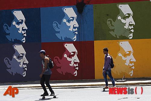 【카라카스 =AP/뉴시스】우고 차베스 전 베네수엘라 대통령의 1주기를 하루 앞둔 4일 카라카스 도심에서 그의 얼굴이 그려진 대형벽화 앞을 두 남자가 스케이트보드를 타고 지나가고 있다.