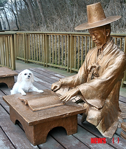 【증평=뉴시스】강신욱 기자 = 17일 충북 증평군 증평읍 율리 삼기저수지 둘레에 설치한 김득신 쉼터에서 강아지 한 마리가 책상에 앞다리를 걸치고 호기심 어린 눈으로 김득신 상을 보고 있다. 2014.03.17.&nbsp; ksw64@newsis.com 