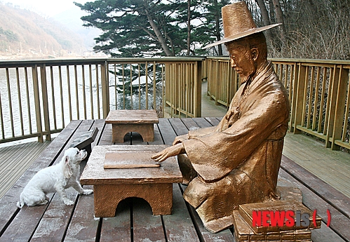 【증평=뉴시스】강신욱 기자 = 17일 충북 증평군 증평읍 율리 삼기저수지 둘레에 설치한 김득신 쉼터에서 강아지 한 마리가 책상 앞에 앉아 김득신 상을 바라보고 있다. 2014.03.17.&nbsp; ksw64@newsis.com 