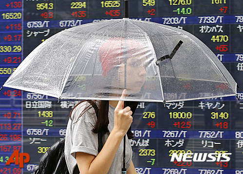 【도쿄=AP/뉴시스】7일 일본 도쿄의 한 증권사 시황판 앞을 우산을 받쳐든 시민이 지나고 있다. 2016.06.07 