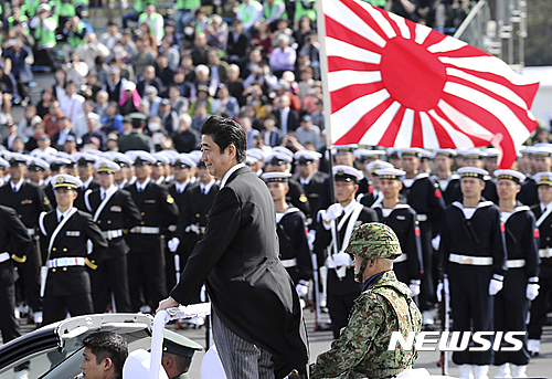 【도쿄=AP/뉴시스】아베 신조(安倍晋三) 일본 총리가 23일 도쿄(東京) 네리마(練馬)구 아사카(朝霞)주둔지에서 열린 육상자위대 사열식에 참석해 오픈카를 타고 행진을 벌이고 있다. 아베 총리 뒤쪽에 한 자위대원이 자위대의 상징인 욱일기를 들고 있다. 2016.10.23.