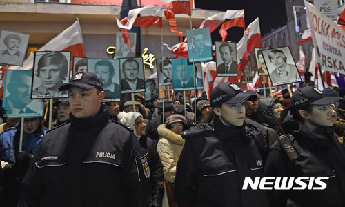 【바르샤바=AP/뉴시스】폴란드 바르샤바 경찰이 13일 반정부 시위대의 행진에 항의하기 위해 1981년 계엄령 당시 민주화운동을 하다 희생된 가족들의 사진을 들고 보도에 서있는 친정부 군중과 시위대의 사이를 막아서서 양측의 충돌을 막고 있다.&nbsp;&nbsp; 