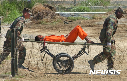 【  AP/뉴시스】 = 쿠바의 관타나모 만에 있는 미해군기지 않의 악명높은 미군감옥에서 미군들이 2002년 아프간출신의  재소자를 들것에 싣고 군사법정으로 이송하는 장면.  트럼프는 이 감옥을 재사용하려 하고 있으며 오바마의  백악관은 지난 1월 17일 이 교도소가 아직도 문을 열고 있어 버락 오바마대통령의 폐쇄계획이 실패했음을 시인했다.     