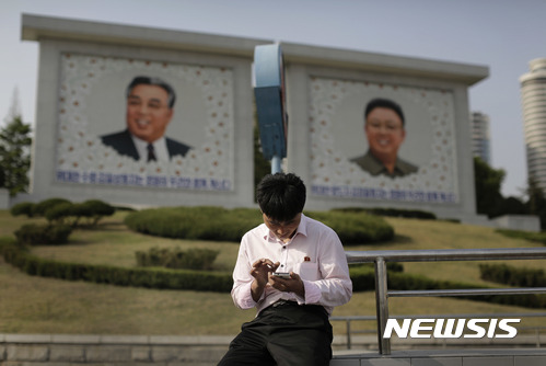 【평양=AP/뉴시스】 북한 남성이 지난 2015년 5월5일 평양에 김일성과 김정일의 대형 초상화 앞에서 스마트폰을 사용하고 있다. 