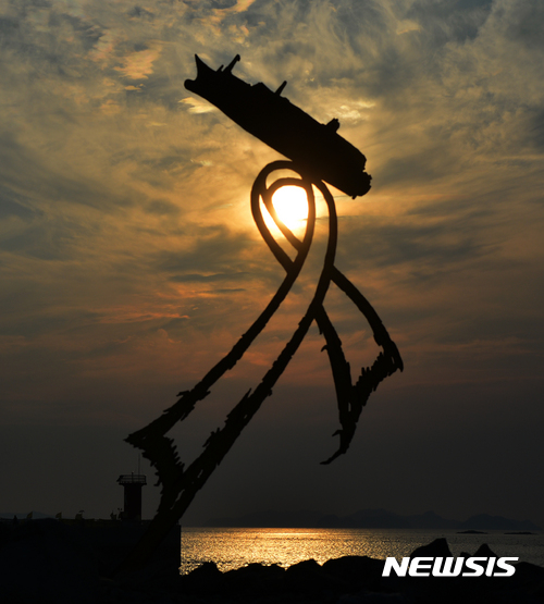【진도=뉴시스】류형근 기자 = 인양된 세월호 목포 항해를 하루 앞둔 30일 오후 기다림의 항구였던 전남 진도군 임회면 팽목항 등대에 세워진 조형물 뒤로 노을이 지고 있다. 팽목항의 가족대기실 등 컨테이너 시설물은 세월호와 함께 목포신항으로 옮겨지며 조형물은 영구 보관될 예정이다. 2017.03.30.&nbsp; hgryu77@newsis.com