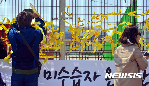【목포=뉴시스】류형근 기자 = 인양된 세월호 입항 사흘째인 2일 오후 전남 목포시 목포신항만 앞에서 세월호 잊지않기 목포지역공동실천회의가 '그립다 보고싶다'라는 주제로 행사를 열고 있는 가운데 추모객들이 세월호가 보이는 철망에 노란리본을 달고 있다. 2017.04.02.&nbsp; hgryu77@newsis.com