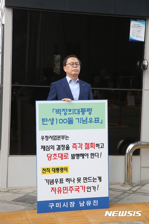 【세종·구미=뉴시스】박홍식 기자 = 남유진 경북 구미시장이 12일 오전 세종시 우정사업본부 본관 앞에서 박정희 전 대통령 탄생 100주년 기념우표 발행을 촉구하는 1인 시위를 하고 있다. 남 시장은 피켓을 들고 "이미 적법한 절차로 결정한 사안을 재심의하는 것은 옳지 않다"며 "기념우표 발행을 당초 계획대로 진행하라"고 촉구했다. 2017.07.12 (사진=구미시 제공) <a href="mailto:photo@newsis.com">photo@newsis.com</a>