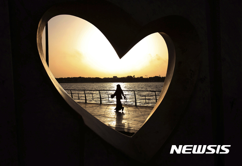 【제다(사우디아라비아)=AP/뉴시스】지난 2014년 5월11일 사우디아라비아 제다에서 전신을 가리는 길고 헐거운 옷을 입은 한 사우디 여성이 홍해 변을 걸어가는 모습이 하트 모양의 조각 사이로 보이고 있다. 사우디의 한 젊은 여성이 배꼽티와 미니스커트를 입고 공공장소를 걷은 모습을 담은 자신의 동영상을 소셜미디어에 게시해 큰 파문이 일고 있다. 2017.7.18