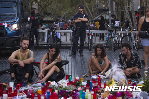 【바르셀로나=AP/뉴시스】 20일 스페인 바르셀로나에서 지난 17일의 차량 테러에 희생된 13명을 추모하는 사람들이 촛불과 꽃들이 놓인 현장에 가만히 앉아 있다. 뒤에 경계를 서고 있는 경찰이 보인다. 2017. 8. 20.