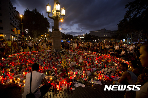 People stand next to candles and flowers placed on the ground, after a terror attack that killed at least 14 people and wounded over 120 in Barcelona, Spain, Sunday, Aug. 20, 2017. (AP Photo/Emilio Morenatti)