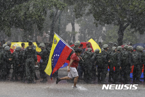  【카라카스=AP/뉴시스】니콜라스 마두로 베네수엘라 대통령의 지지자가 26일(현지시간) 카라카스에서 도열한 군인들 뒤로 지나가고 있다. 정부는 이날 정부에 비판적인 외국 케이블 방송사 지부의 방송중단에 이어 현지 민간 라디오 방송사 2곳의 방송도 중단했다. 2017.08.27