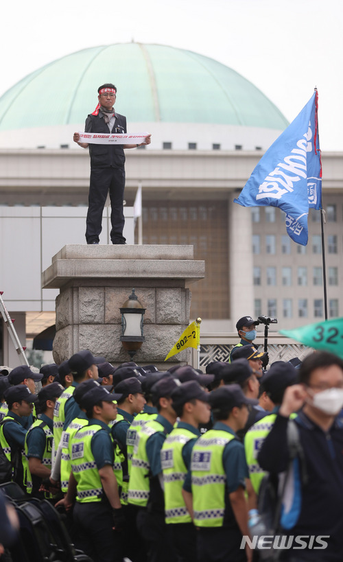 【서울=뉴시스】임태훈 기자 = 21일 오후 최저임금 산입범위 확대 개악 저지를 위한 결의대회를 마친 전국민주노동조합총연맹 조합원이 서울 여의도 국회 정문 기둥에 올라 최저임금 개악논의 중단을 촉구하는 손 팻말을 들고 있다. 2018.05.21. taehoonlim@newsis.com