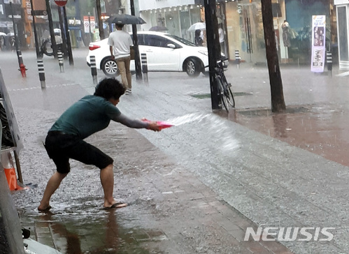 【대구=뉴시스】이통원 기자 = 30일 오후 대구 중구 동성로에 폭우와 함께 우박이 쏟아진 가운데 한 상인이 매장으로 밀려드는 물을 쓰레받이로 퍼내고 있다. 2018.05.30.tong@newsis.com