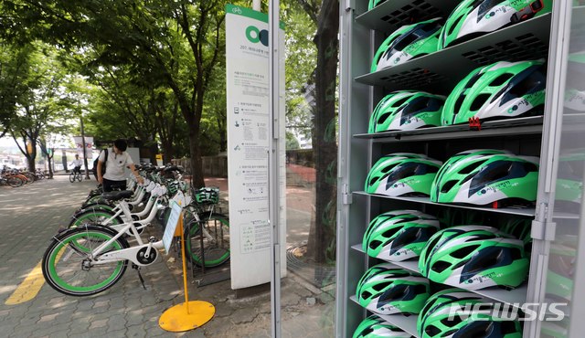 【서울=뉴시스】고범준 기자 = 서울시설공단이 지난 19일 공공자전거 '따릉이'를 이용할 때 안전모 무료 대여 사업을 한 달간 시범 운영한다고 밝혔다. 따릉이 이용자들의 안전모 착용이 의무화되는 9월을 앞두고 여의도 지역 따릉이 대여소 30곳에서 안전모 500개를 시범 대여해 준다.사진은 20일 오후 서울 영등포구 여의나루역 인근 안전모 보관소 앞에서 시민들이 따릉이와 안전모를 이용하는 모습. 2018.07.20. bjko@newsis.com