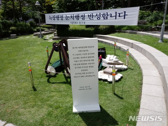 【서울=뉴시스】 손대선 기자 = 서울 중구가 30일 서울시청 광장 앞에 설치했다가 철거한 무더위 그늘막을 구청 잔디광장으로 옮겨 전시하고 있다.  중구는 그늘막 앞에 표지판을 세워 철거의 이유를 설명하고 있다.    sds1105@newsis.com   