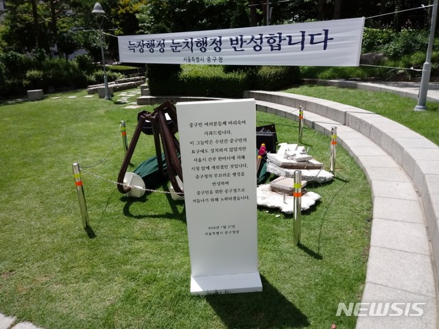 【서울=뉴시스】 손대선 기자 = 서울 중구가 30일 서울시청 광장 앞에 설치했다가 철거한 무더위 그늘막을 구청 잔디광장으로 옮겨 전시하고 있다. 중구는 그늘막 앞에 표지판을 세워 철거의 이유를 설명하고 있다.&nbsp; sds1105@newsis.com&nbsp; 