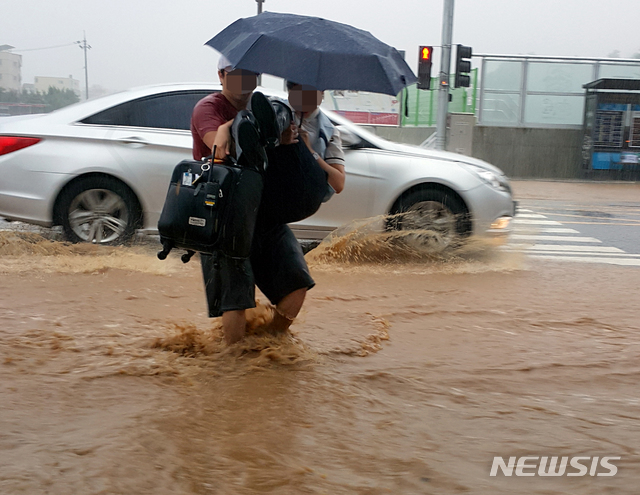 【강릉=뉴시스】김경목 기자 = 6일 오전 강원 강릉시에 호우경보가 발효 중인 가운데 한 시민이 KTX 승무원을 안고 토사가 썩인 빗물로 침수된 횡단보도를 건너고 있다. 2018.08.06.&nbsp; photo31@newsis.com