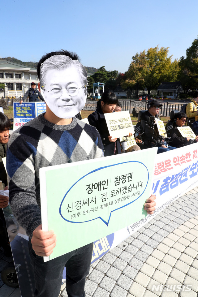 【서울=뉴시스】조성봉 기자 = 17일 오전 서울 종로구 청와대 인근 분수대 앞에서 열린 장애인 참정권 보장 약속 이행 촉구 기자회견에서 문재인 대통령의 가면을 쓴 참가자가 '참정권 보장 약속 이행'을 요구하는 피켓을 들고 있다 .2018.10.17.suncho21@newsis.com