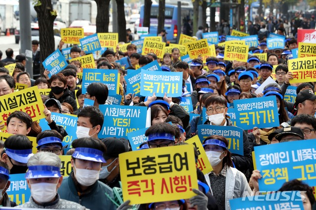 【서울=뉴시스】조성봉 기자 = 23일 오후 서울 종로구 정부서울청사 앞에서 열린 장애인직업재활 시설 최저임금 국가책임 요구집회에서 참가자들이 '최저임금 국가책임' 손피켓을 들고 구호를 외치고 있다. 2018.10.23.suncho21@newsis.com