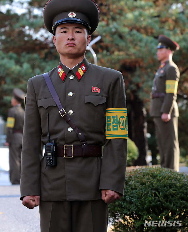 【판문점=뉴시스】사진공동취재단 = 지난 25일 오후 1시 판문점 공동 경비구역(JSA) 안 모든 화기와 탄약 초소를 철수했다. 26일 북측 판문점 뒷편 통일각에서 노랑색 바탕에 녹색으로 적힌 '판문점 민사경찰 27'이라는 완장을 찬 채 북한 군인이 경비를 서고 있다. 두 주먹을 힘껏 꽉 쥔 손에는 굳은살이 보인다. 2018.10.28. photo@newsis.com