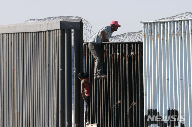 【티후아나=AP/뉴시스】중미 출신 남성이 14일(현지시간) 미국 샌디에이고 과 멕시코 티후아나 사이에 있는 국경구조물 위로 올라가고 있다. 2018.11.