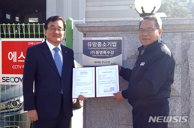 【창원=뉴시스】 홍정명 기자 = 27일 경남 진주시 ㈜동명특수강 정문에서 BNK경남은행 서부영업본부 김영모(왼쪽) 상무가 이성갑 대표에게 '유망중소기업' 현판과 인증서를 전달하고 있다.2018.11.27.(사진=BNK경남은행 제공) photo@newsis.com