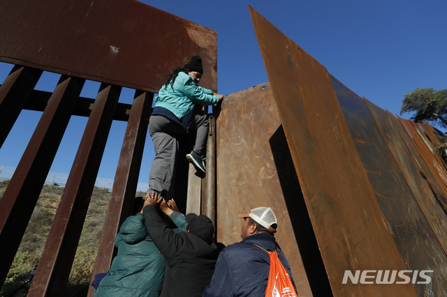 【티후아나=AP/뉴시스】 12일(현지시간) 한 여성 온두라스 이민자가 동료들의 도움으로 멕시코 티후아나의 멕시코-샌디에고 장벽을 넘고 있다. 시간이 오래 걸리는 망명 신청 절차를 피하려는 이들은 장벽을 넘어 미국 국경 경비대에 자수해 망명 절차를 밟는다. 2018.12.13.
