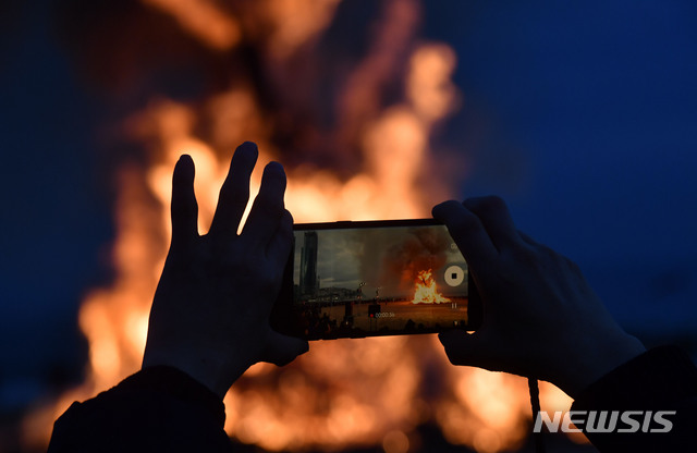 【부산=뉴시스】 하경민 기자 = 정월대보름인 19일 오후 부산 해운대해수욕장에서 액운을 씻어내고 건강과 풍요를 기원하는 달집이 활활 타고 있는 가운데 시민이 휴대전화로 이를 담고 있다. 2019.02.19. yulnetphoto@newsis.com