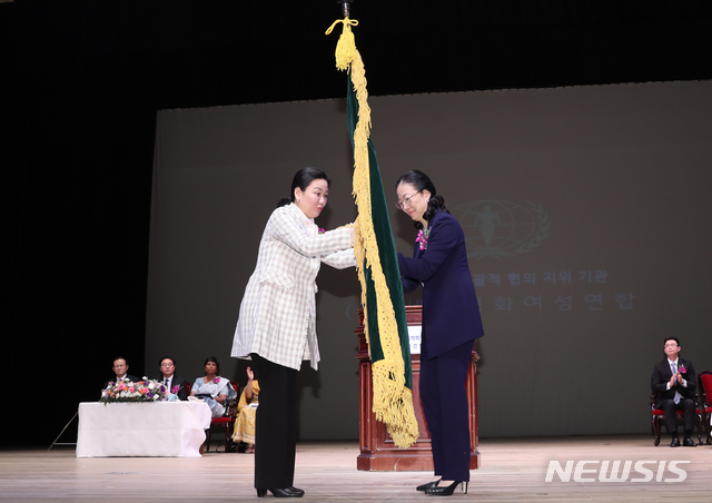 【서울=뉴시스】조수정 기자 = 6일 오후 서울 광진구 능동 유니버설아트센터에서 열린 세계평화여성연합 문연아 세계회장 이임, 문훈숙 세계회장 겸 한국회장 취임식에서 문연아(왼쪽) 전 회장이 문훈숙 신임 회장에게 깃발을 전달하고 있다. 2019.03.06. chocrystal@newsis.com