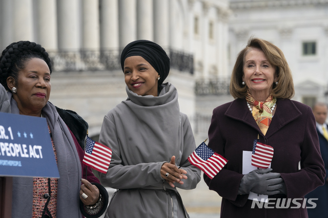 【워싱턴=AP/뉴시스】 최초의 무슬림 여성 하원의원인 일한 오마르(가운데)와 하원의장인 낸시 펠로시(오른쪽)가 성조기를 들고 웃고 있다. 펠로시 의장은 13일(현지시간) 9.11 테러 영상을 게시한 도널드 트럼프 대통령을 비난하며 "9.11의 기억은 신성하다. 관련한 그 어떤 논의도 경건하게 이뤄져야 한다"고 지적했다. 트럼프 대통령은 12일 트위터에 오마르 의원의 의회 연설 장면과 9.11 테러 영상을 함께 게시했다. 2019.04.14.