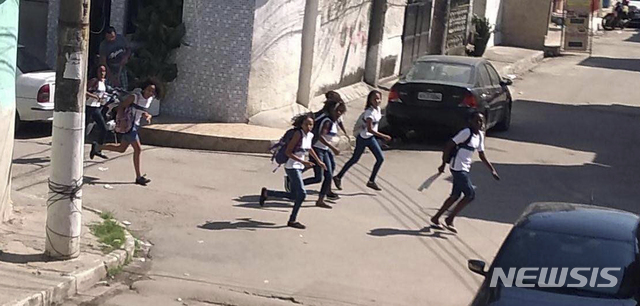 【리우데자네이루= AP/뉴시스】 브라질 경찰이 마약조직으로 의심되는 저격수들과 대치하면서 리우 시내 빈민가에서 총격전을 벌인 올 5월 6일 학생들이 급히 달아나고 있다. 새 리우 주지사는 경찰에게 무기 사용은 물론, 용의자를 살해할 권한을 부여해 경찰의 총기사용의 희생자는 더 늘어났다고 당국은 밝혔다.