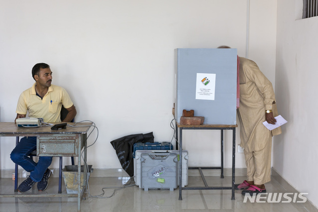 A polling official, left waits for confirmation of successful polling as an Indian man votes in the seventh and final phase of national elections in Dharmsala, India, Sunday, May 19, 2019. Sunday's polling wraps up a 6-week-long long, grueling campaign season with Prime Minister Narendra Modi's Hindu nationalist party seeking reelection for another five years. Counting of votes is scheduled for May 23. (AP Photo/Ashwini Bhatia)