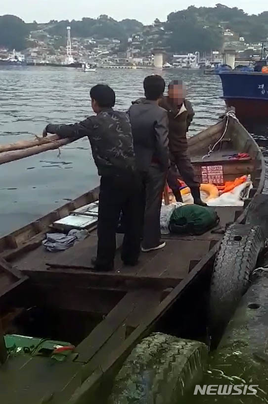 【서울=뉴시스】 삼척 북한 목선 파장이 갈수록 커지고 있는 21일 지난 15일 오전 6시 50분, 삼척항 방파제에 북한 어선이 왔다는 신고에 삼척 파출소 경찰들이 목선을 타고 온 북한 주민들을 조사하고 있다.&nbsp; 해경은 19분이 지난 7시 9분에 첫 보고서를 청와대, 국정원, 합참 등에 북한 어선이 자체 동력으로 삼척항에 입항했다고 보고 했다. 하지만 군은 17일 첫 발표에서 어선 발견 지점을 '삼척항 인근'이라고만 했고, 표류라고 명시해, 자체 동력으로 배가 움직인 것도 숨겨 논란이 되고 있다. 2019.06.21. (사진= 독자 제공) photo@newsis.com