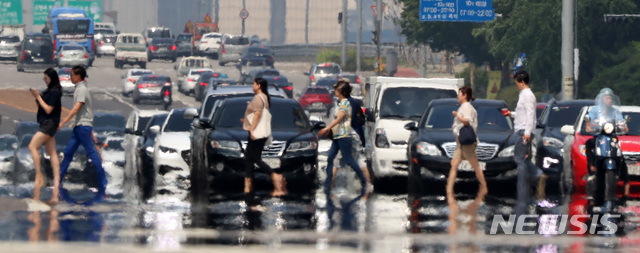【서울=뉴시스】이영환 기자 = 서울과 경기 등 일부지역에 올해 처음으로 폭염경보가 발효된 5일 오후 시민들이 아지랑이가 피어오르고 있는 서울 영등포구 여의도 환승센터 신호등을 건너고 있다. 2019.07.05.&nbsp; 20hwan@newsis.com