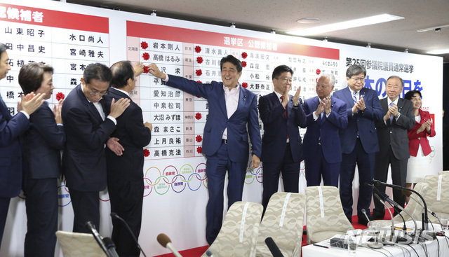 Japanese Prime Minister Shinzo Abe, center, smiles with his party's lawmakers in front of red rosettes on the names of his Liberal Democratic Party's winning candidates during ballot counting for the upper house elections at the party headquarters in Tokyo, Sunday, July 21, 2019. Prime Minister Abe's ruling coalition appeared certain to hold onto a majority in Japan's upper house of parliament, with exit polls from Sunday's election indicating he could even close in on the super-majority needed to propose constitutional revisions.(AP Photo/Koji Sasahara)