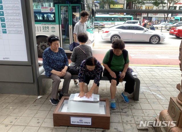 한 시민이 모란역 버스정류장에 비치한 얼음에 손을 올려놓고 더위를 식히고 있다. (사진제공=성남시)