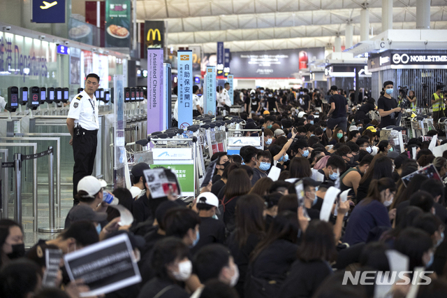 【홍콩=AP/뉴시스】 홍콩 국제공항에서 13일 2층 출국 홀을 점거한 시위대가 수하물 카트를 몰고와 출국 게이트 앞을 봉쇄한 가운데 한 공항 보안요원이 게이트 앞에서 뒷짐 지고 이를 보고 있다. 이날 공항 당국은 시위대가 1층 입국장과 2층을 다시 점거하자 2층의 항공사 체크인 서비스를 오후 5시 무렵 전면 중단했다. 시위대가 출국 게이트를 막아선 것은 그 다음 상황으로 보인다. 2019. 8. 13.  