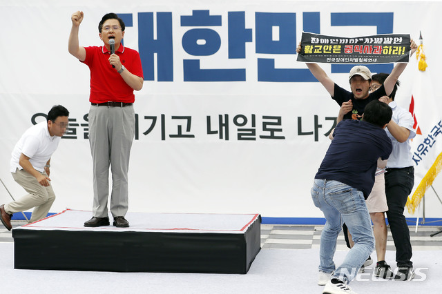 【서울=뉴시스】최동준 기자 = 자유한국당 황교안 대표가 24일 서울 종로구 세종문화회관 앞에서 열린 문재인 정권 국정운영 규탄 집회에서 발언을 하자 전국장애인차별철폐연대 피켓을 든 남성이 단상에 올라 황 대표에게 항의하고 있다. 2019.08.24. photocdj@newsis.com