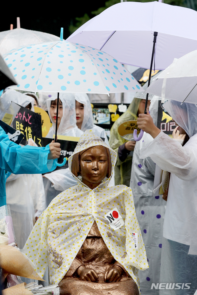 【서울=뉴시스】김병문 기자 = 4일 오후 서울 종로구 구 일본대사관 앞에서 열린 일본군성노예제 문제해결을 위한 1403차 정기 수요시위에 참석한 학생들이 비가 오자 소녀상에게 우산을 씌워주고 있다. 2019.09.04. dadazon@newsis.com