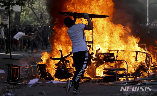 【산티아고=AP/뉴시스】21일(현지시간) 칠레 수도 산티아고에서 한 남성이 도로를 막아 놓은 불붙은 의자와 테이블에 모니터를 집어 던지고 있다. 지하철 요금 인상으로 촉발된 반정부 시위가 산티아고를 비롯, 칠레 전역에서 이어지는 가운데 지금까지 11명이 사망한 것으로 알려졌다. 세바스티안 피녜라 대통령은 "지금 칠레는 전쟁 중"이라며 강경 대응을 시사한 바 있다. 2019.10.22.