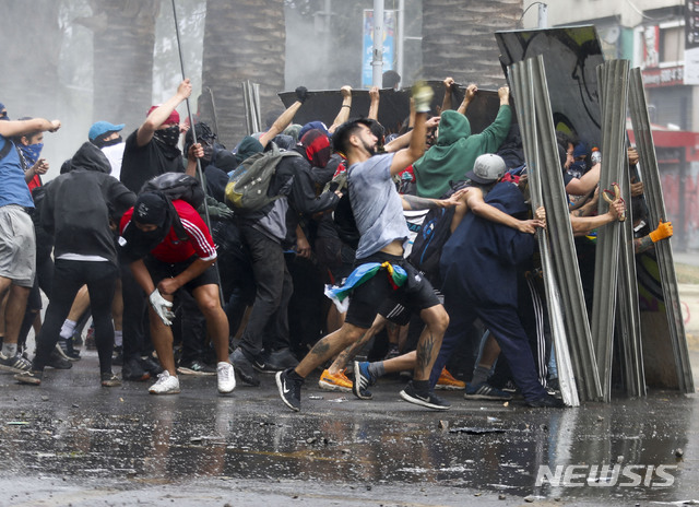 【산티아고=AP/뉴시스】23일(현지시간) 칠레 수도 산티아고에서 중앙노동조합총연맹(CUT)이 주도하는 이틀간의 총파업이 시작되면서 반정부 시위대가 금속판으로 경찰의 물대포를 막으며 시위하고 있다. 세바스티안 피녜라 대통령이 시위대의 분노를 이해하지 못한 점을 사과하고 연금과 최저임금 인상 등 대책을 내놨으나 시위는 줄지 않고 있으며 지금까지 18명이 숨진 것으로 파악됐다. 2019.10.24. 