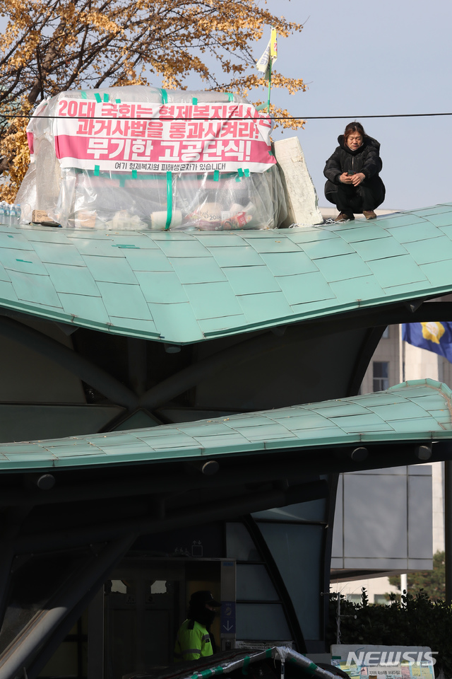 [서울=뉴시스] 고승민 기자 = 형제복지원 진상규명을 위한 과거사법 통과를 촉구하며 22일째 국회 앞에서 고공 단식농성을 벌이고 있는 복지원 생존자 최승우 씨가 27일 서울 여의도 국회의사당역 6번출구 위에 홀로 앉아 있다.  2019.11.27.kkssmm99@newsis.com