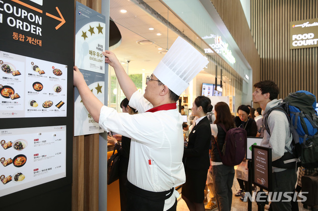 [서울=뉴시스] 인천공항 제 2터미널 아워홈 푸디움에서 조리사가 위생등급제 인증 현판을 부착하고 있다. 