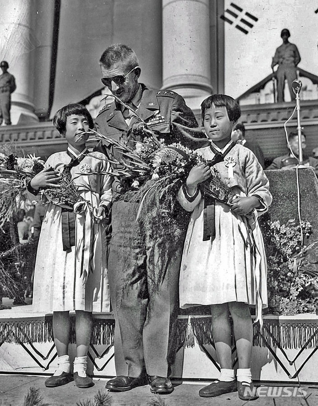 [서울=뉴시스] 1945년 10월 20일 중앙청 앞에서 열린 서울시민 주최 연합국환영대회에서 주한 미군 사령관 하지 중장, 아놀드 군정장관에게 증정할 꽃다발 들고 나온 수송국민학교 5학년 양정희(楊貞熙)와 정인경(鄭仁卿) 학생이 하지 중장과 기념촬영을 하고 있다. (사진=돈 오브라이언 flickr) 2020.02.09. (* 위 사진은 재배포, 재판매, DB 및 활용을 금지합니다.)photo@newsis.com