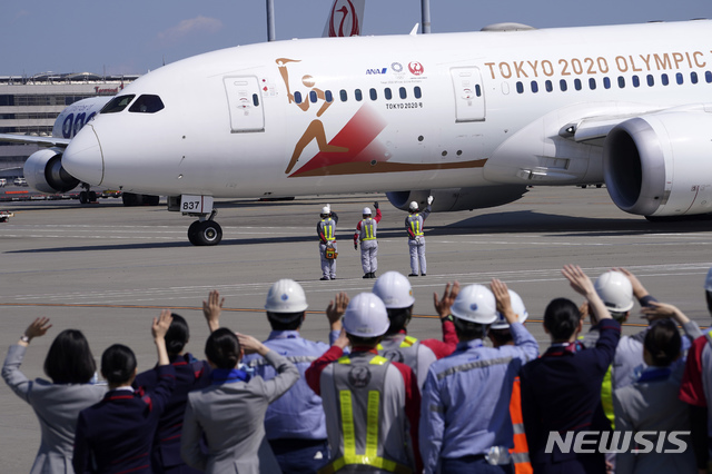 [도쿄=AP/뉴시스]18일 일본 도쿄 하네다 국제공항 활주로에서 지상 근무자들이 2020 도쿄 올림픽 성화 운반차 그리스로 떠나는 일본 항공 소속 특별기를 향해 손을 흔들며 환송하고 있다. 2020.03.18.